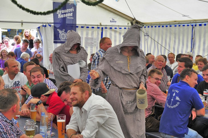 Beim Einzug ins Bullacher Kirchweihzelt sparten die „Mönche“ nicht mit Weihwasser aus dem Bierkrug (links). Dass die Frauen draußen bleiben mussten, nahmen diese Damen gelassen