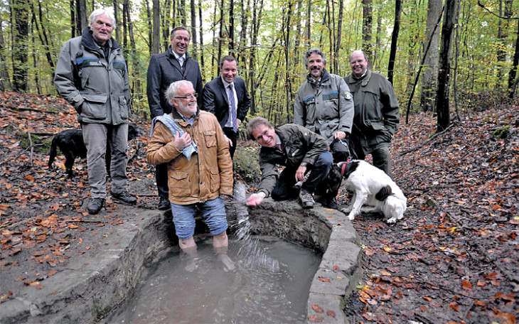 Nur Andreas Ellner, Rückersdorfer Bürgermeister-Stellvertreter, war gestern so tapfer, barfuß in das Becken des Zeller Brünnleins zu steigen. Die Landräte Alexander Tritthart (Erlangen-Höchstadt) und Armin Kroder (Nürnberger Land) – hinter ihm im Bild – blieben lieber trocken. Rechts vorne kniet Roland Blank vom Nürnberger Forstbetrieb. Foto: Sichelstiel