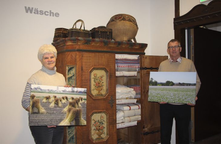 Betty Püntzner und Dieter Sopper präsentieren im Heimatmuseum neben der feinen Leinenwäsche im historischen Bauernschrank Bilder von blühendem Flachs und den geernteten, zu Garben gebundenen Pflanzen.