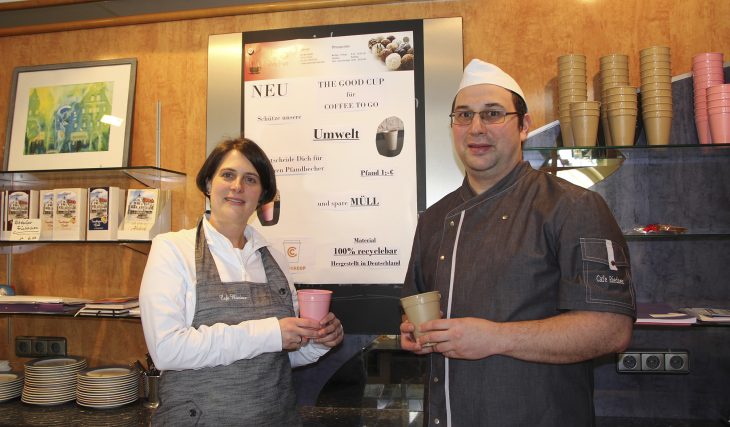 Christina und Johannes Krasser vor dem Info-Poster zum neuen Mehrweg-Becher-Angebot. Die beigen und rosa Kunststoffbehälter sind zu 100 Prozent biologisch abbaubar und werden von der Kundschaft prima angenommen.