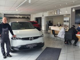 Erich Schwemmer (für das Bild kurz ohne Maske) mit dem Mazda-Elektrofahrzeug MX 30, das bei Auto Schwemmer in Weißenbrunn selbstverständlich auch Probe gefahren werden kann; rechts im Bild Verkaufsberater Selami Dönek im Kundengespräch.