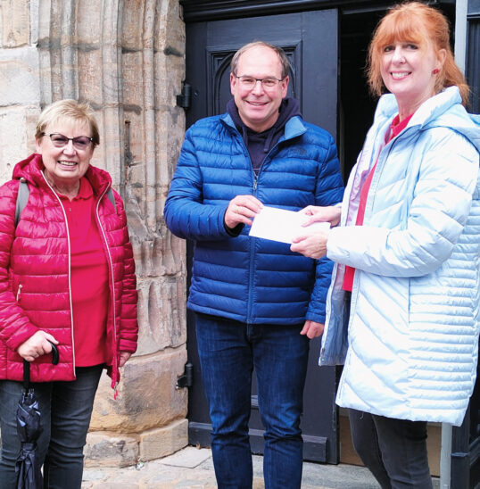 Das Bild zeigt die Stadtführerinnen Alena Popp und Christl Hanisch-Gerstner bei der Spendenübergabe an Pfarrer Jan-Peter Hanstein.