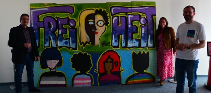 Freuen sich, dass das Graffiti-Kunstwerk der Jugendlichen nun der Öffentlichkeit präsentiert werden kann (v. l.): Büchereileiter Andreas Reichel, Laufs Zweite Bürgermeisterin Nina Bezold und KJR-Vorsitzender Maurizio Schneider.
