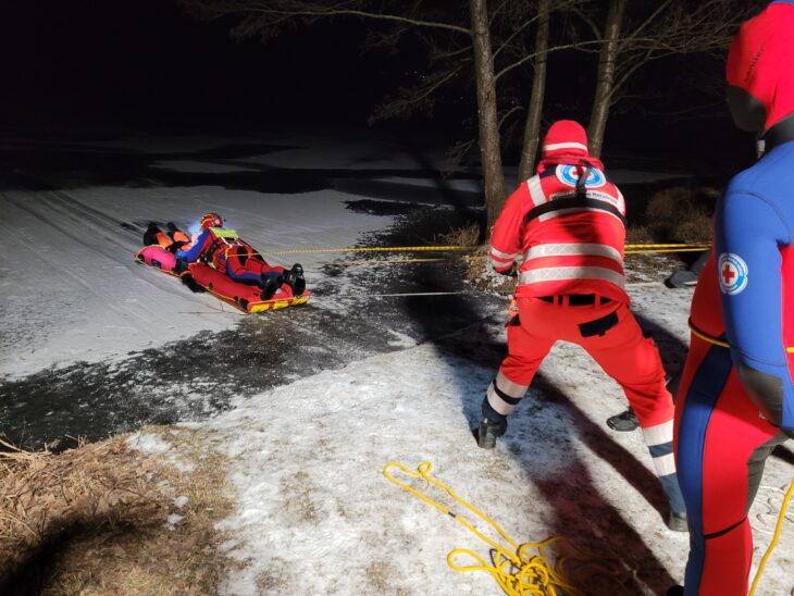 Mit einem Eisrettungsschlitten, einer Art verstärkte Luftmatratze, holen die Retter eine eingebrochene Person an Land.