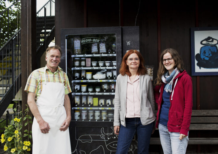 Ein Beispiel eines geförderten Projektes: Franziska Distler und Verena Loibl von der Öko-Modellregion (von rechts) zusammen mit dem Chef der Käserei Münzinghof, Michael Fick, vor dem Verkaufsautomaten Regio-Box.