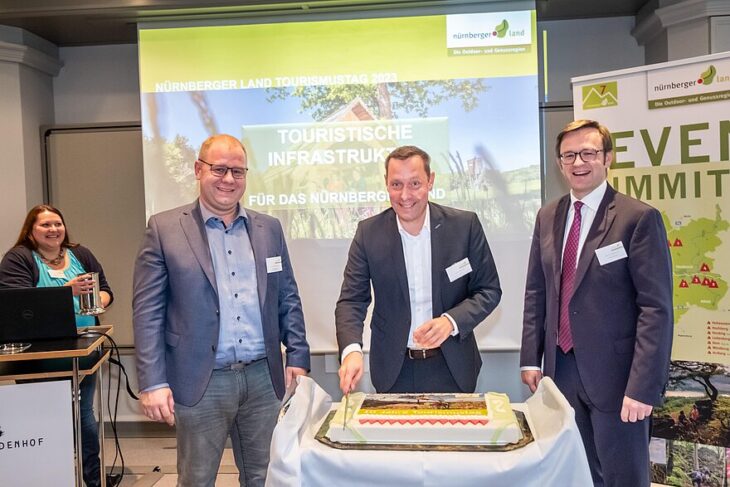 Landrat Armin Kroder (Mitte) schneidet die „Geburtstagstorte“ gemeinsam mit Armin Haushahn, dem Bürgermeister von Pommelsbrunn (links), und Achim Stötzner, dem Geschäftsführer des Lindenhofs (rechts), an.
