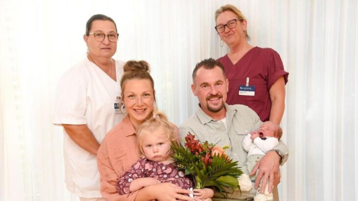 Gesundheits- und Krankenpflegerin Gabi Drube (links) und Hebamme Barbara Kött (rechts) gratulieren der jetzt vierköpfigen Familie (Mama Sabrina, Papa Felix, Tochter Sophia und „Schnapszahl“-Baby Leonardo) mit einem Blumenstrauß.