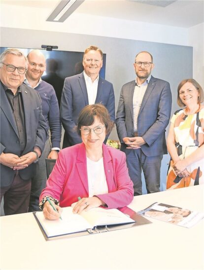Die Regionalbischöfin Elisabeth Hann von Weyhern trägt sich ins Ehrenbuch der Lebenshilfe Nürnberger Land ein. Von der Lebenshilfe Nürnberger Land sind der Vorsitzende Gerhard John, Geschäftsführer Dennis Kummarnitzky, der Vorsitzende des Stiftungsvorstands, Norbert Dünkel, Dekan Tobias Schäfer und Pfarrerin Gabriele Geyer dabei (stehend von links).