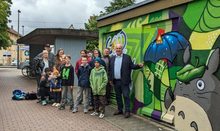 Kulturamtsleiterin Marion Stiegler, Graffiti-Künstler Carlos Lorente (in der Hocke), Juz-Leiterin Ellen Seegebarth, Martin Knorr von den Stadtwerken und Bürgermeister Klaus Hacker mit den Jugendlichen vor einem der beiden bemalten Trafo-Häuschen an der S-Bahn-Station Steinberg.