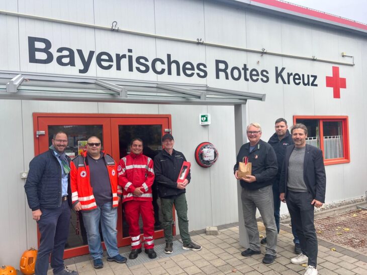 Das Bild zeigt den neuen AED am Schnaittacher Rotkreuzhaus, umrahmt von Frank Pitterlein (1. v.l.), Stefan Frisch und Sven Eichhorn (3. und 4. v.r.) sowie Markus Deyhle (1.v.r.) und weiteren BRK-Vertretern.