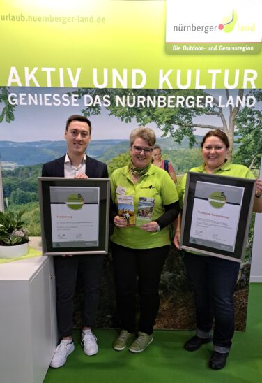 Lukas Schmidt vom Tourismusverband Franken präsentiert das Zertifikat Qualitätswein Wanderbares Deutschland für den Frankenweg. Die Mitarbeiterinnen vom Nürnberger Land Tourismus Petra Hofmann und Saskia Sörgel freuen sich über die Auszeichnung des Frankenalb Panoramawegs (von links).