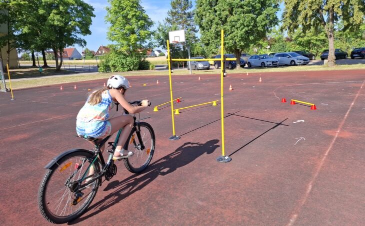 Stangen in gebückter Haltung durchfahren – nur eine von vielen Aufgaben beim Radltraining durch einen Parcours an der Grundschule Neunkirchen.