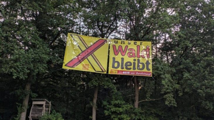 Die Trassengegner planen eine Aktion mit gelben und roten Rauchfackeln am großen Banner am Waldrand an der A3.