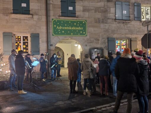 Auf dem Foto sieht man unter anderem den Gemeinderat bei der Eröffnung des sogenannten Adventsfensters an einer Hausmauer.