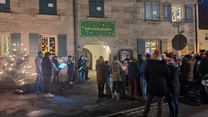 Auf dem Foto sieht man unter anderem den Gemeinderat bei der Eröffnung des sogenannten Adventsfensters an einer Hausmauer.