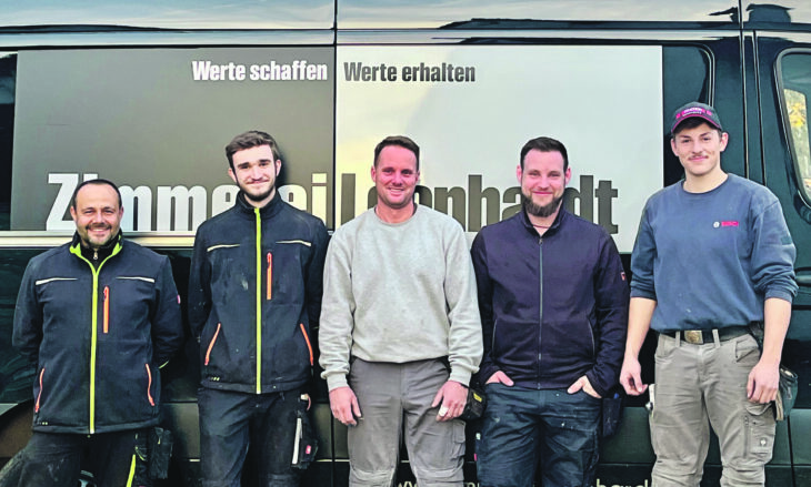 Fünf Mitarbeiter der Firma Zimmerei Leonhardt aus Altdorf zeigen sich vor ihrem Firmenlogo
