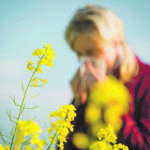 nießende Frau mit Taschentuch vor Gräsern