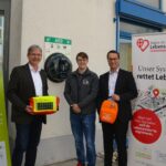 Hewa-Geschäftsführer Harald Kiesl freut sich mit Tobias Buchholz, Projektkoordinator von „Nürnberger Land schockt“, und Bürgermeister Robert Ilg (v. rechts) über den neuen Defi-Standort am Eingang zum Hewa-Kundenzentrum in der Wilhelm-Ulmer-Straße.