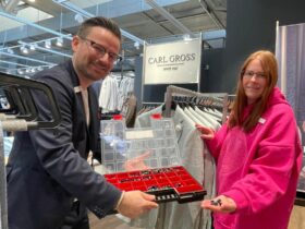 Lisa Herbst überprüft Kleiderbügel mit Etiketten – Ordnung und Qualitätskontrolle gehören zu ihren Aufgaben bei Création Gross in Hersbruck. Angeleitet wird sie von Stefan Hellmer, der ihr auch als „Betriebspate“ für alle Fragen im Betrieb zur Seite steht.