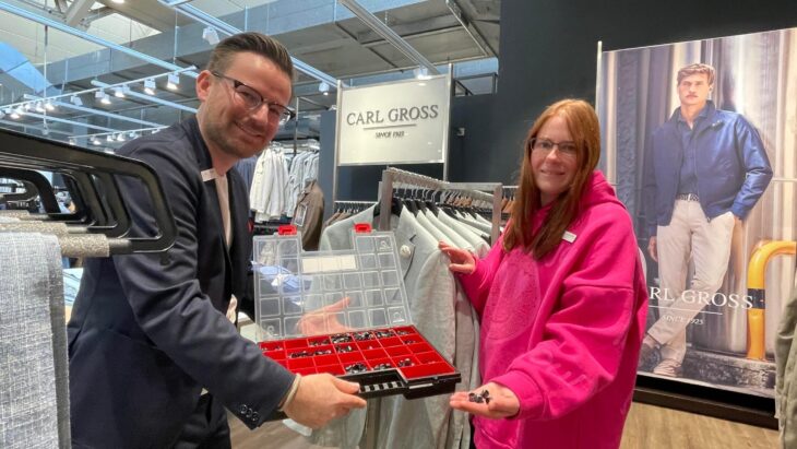 Lisa Herbst überprüft Kleiderbügel mit Etiketten – Ordnung und Qualitätskontrolle gehören zu ihren Aufgaben bei Création Gross in Hersbruck. Angeleitet wird sie von Stefan Hellmer, der ihr auch als „Betriebspate“ für alle Fragen im Betrieb zur Seite steht.