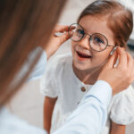 kleines Mädchen mit Brille, die von einer Frau aufgesetzt wird
