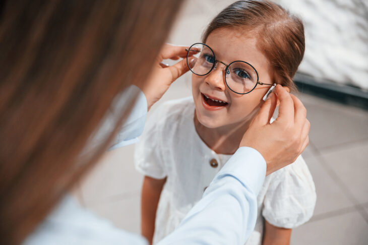 kleines Mädchen mit Brille, die von einer Frau aufgesetzt wird