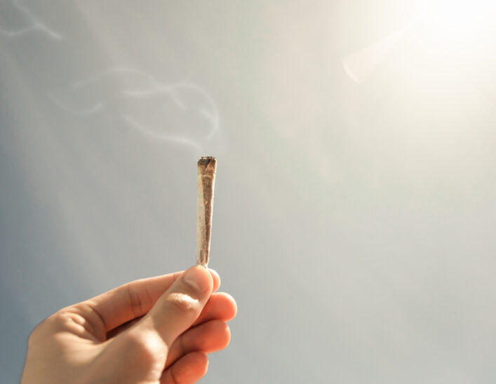 man-holding-a-lit-joint-of-marijuana-with-a-soft-sky-and-shiny-sun-in-the-background-cigarette-with-smoke-right-and-top-copy-space