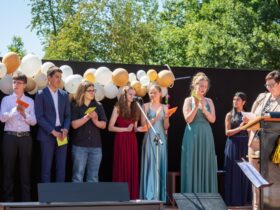 Schulleiterin Birgit Seidl (am Pult) zeichnet die besten Schülerinnen und Schüler des Jahrgangs aus (von links): Eleanor Gheorge, Rahoz Nuri, Moritz Krauß, Alexandru Mágurean, Thea Völkel, Antonia Paul , Milena Lukinskiy und Kristal Singh.